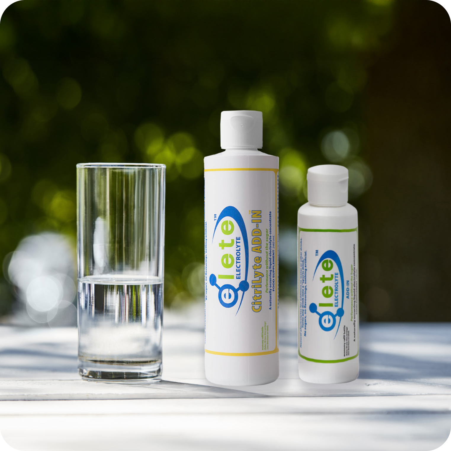 Two bottles of natural electrolyte concentrate and a glass of water on an outdoor table