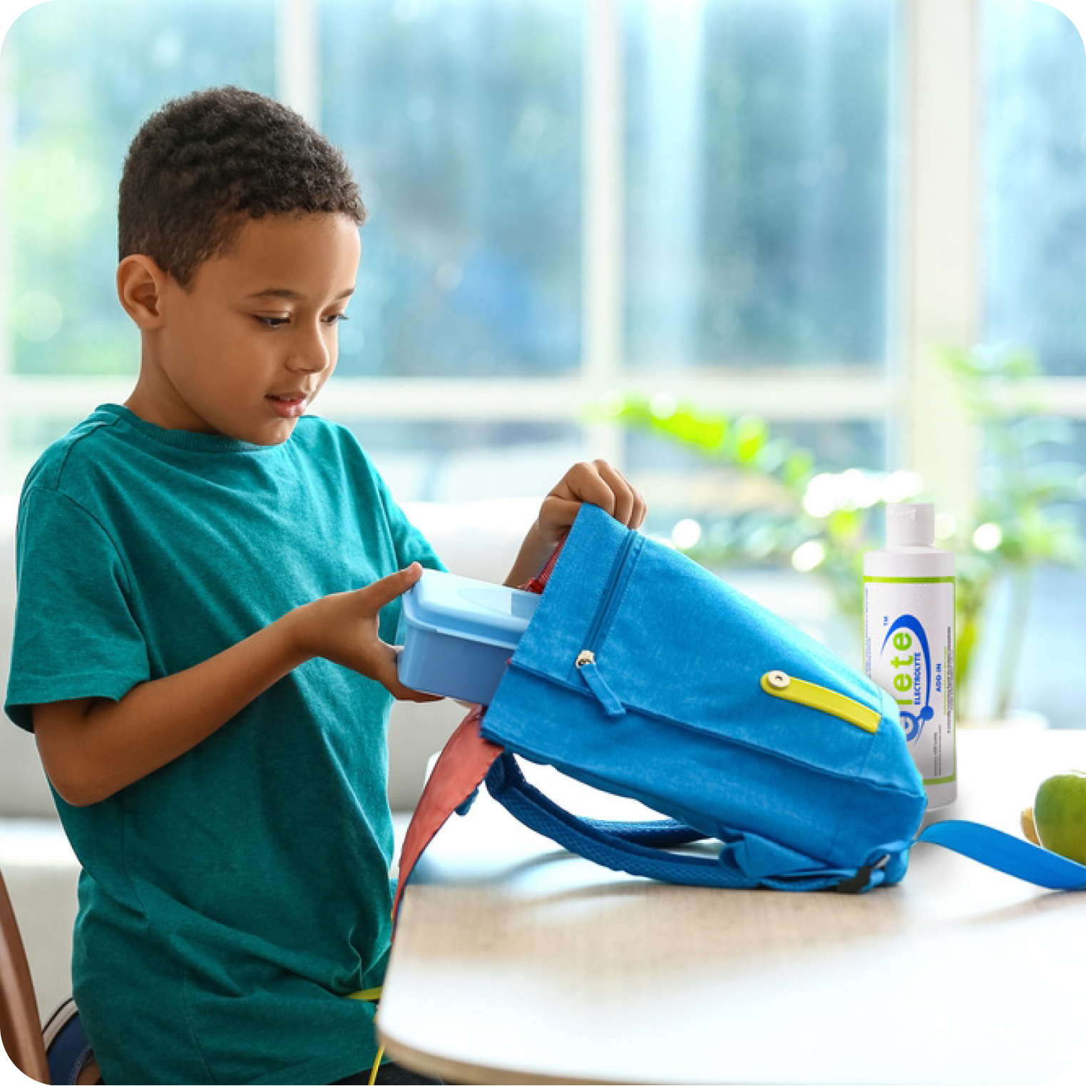 Child packing lunchbox into blue backpack with electrolyte concentrate bottle on table