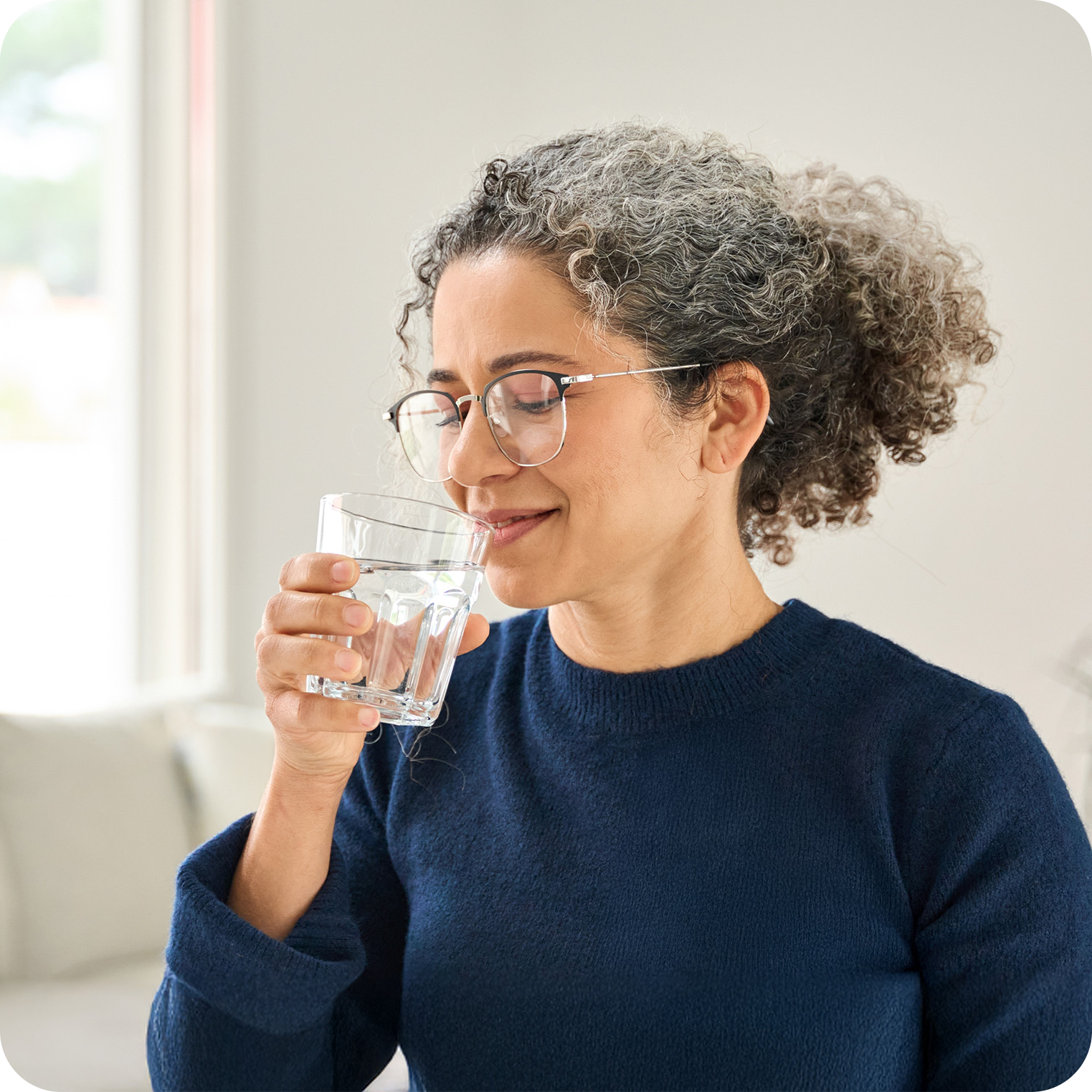 Smiling woman in blue sweater drinking a glass of water for natural hydration