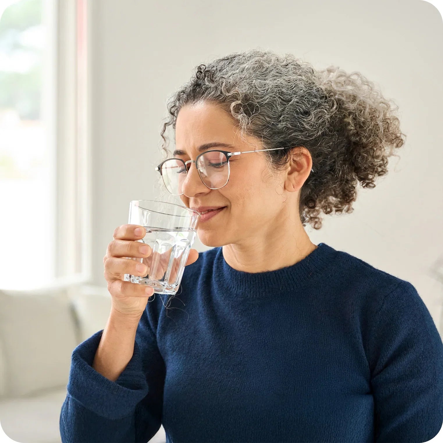 Smiling woman in blue sweater drinking a glass of water for natural hydration