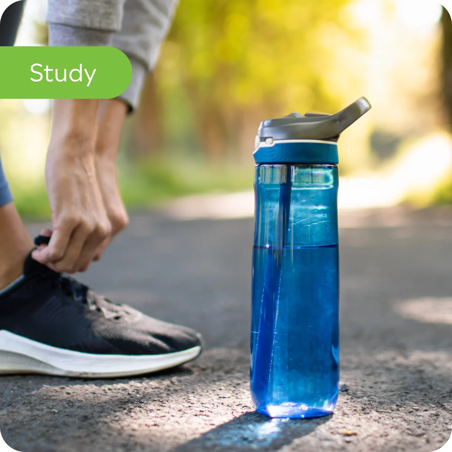 Clear blue water bottle with electrolyte drink on a path, person tying running shoes
