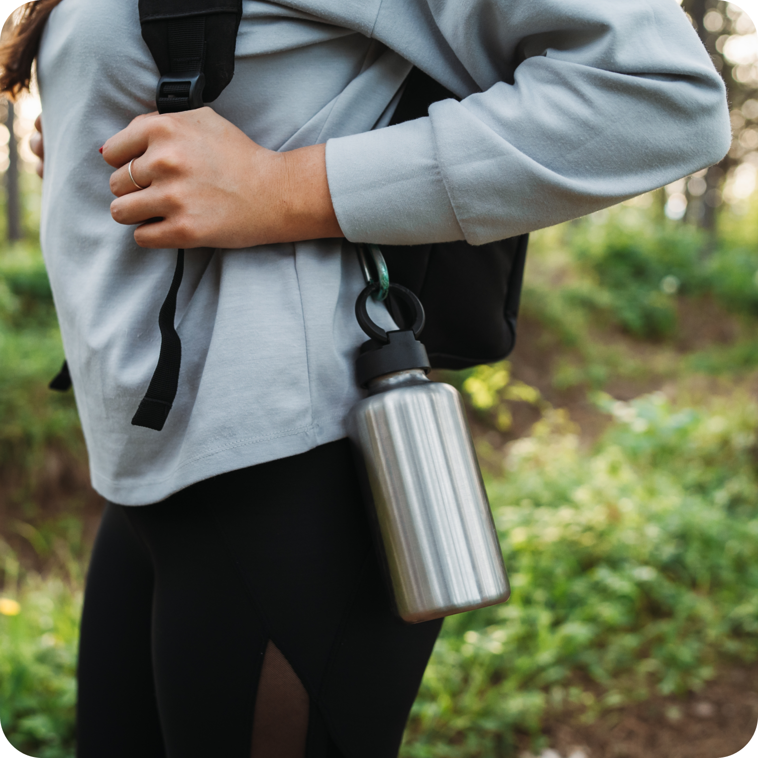 Close up of person outdoors with a stainless steel water bottle attached to a backpack, promoting hydration and electrolyte balance during exercise or hiking.
