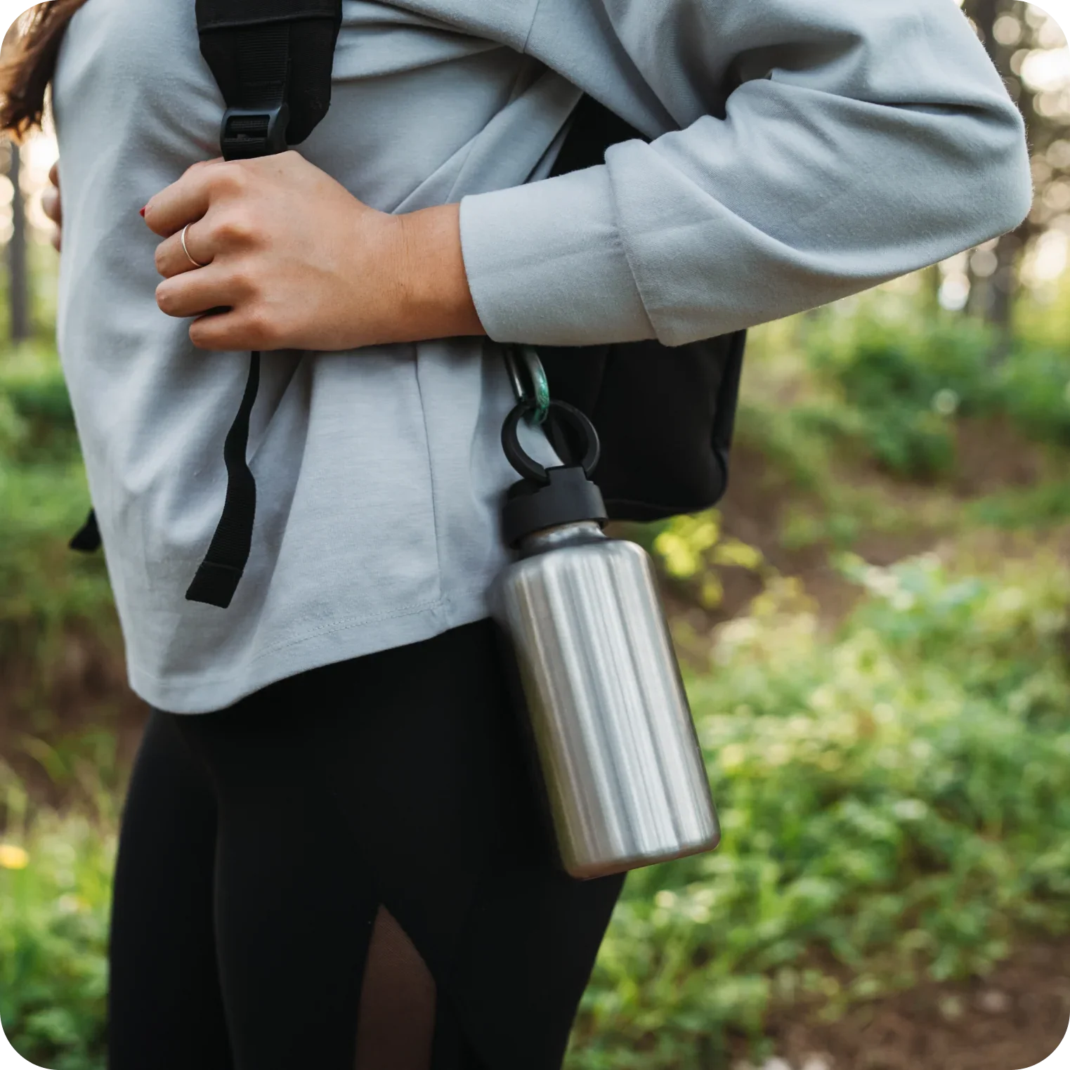 Close up of person outdoors with a stainless steel water bottle attached to a backpack, promoting hydration and electrolyte balance during exercise or hiking.