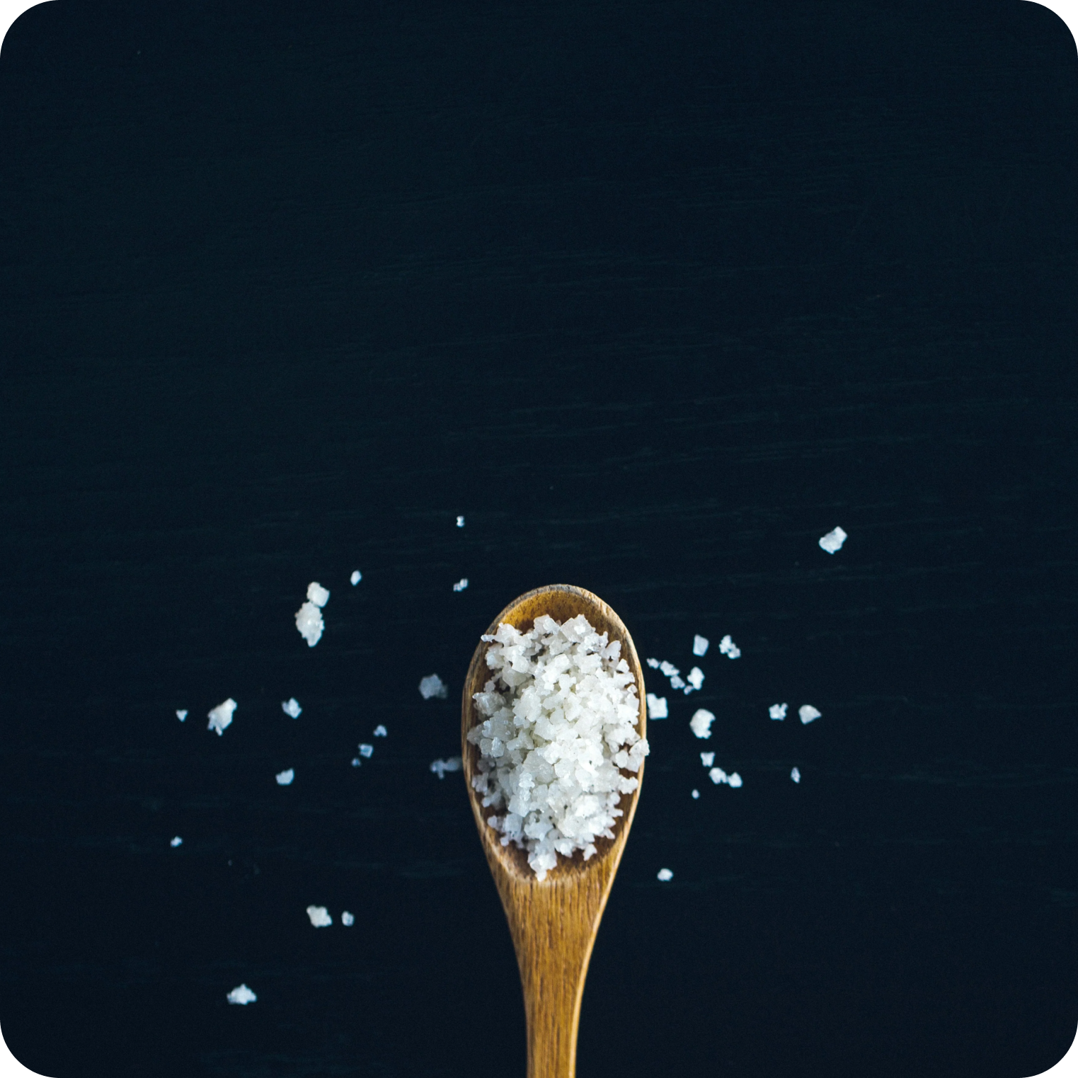 Natural sea salt crystals on wooden spoon, source of electrolytes, dark background