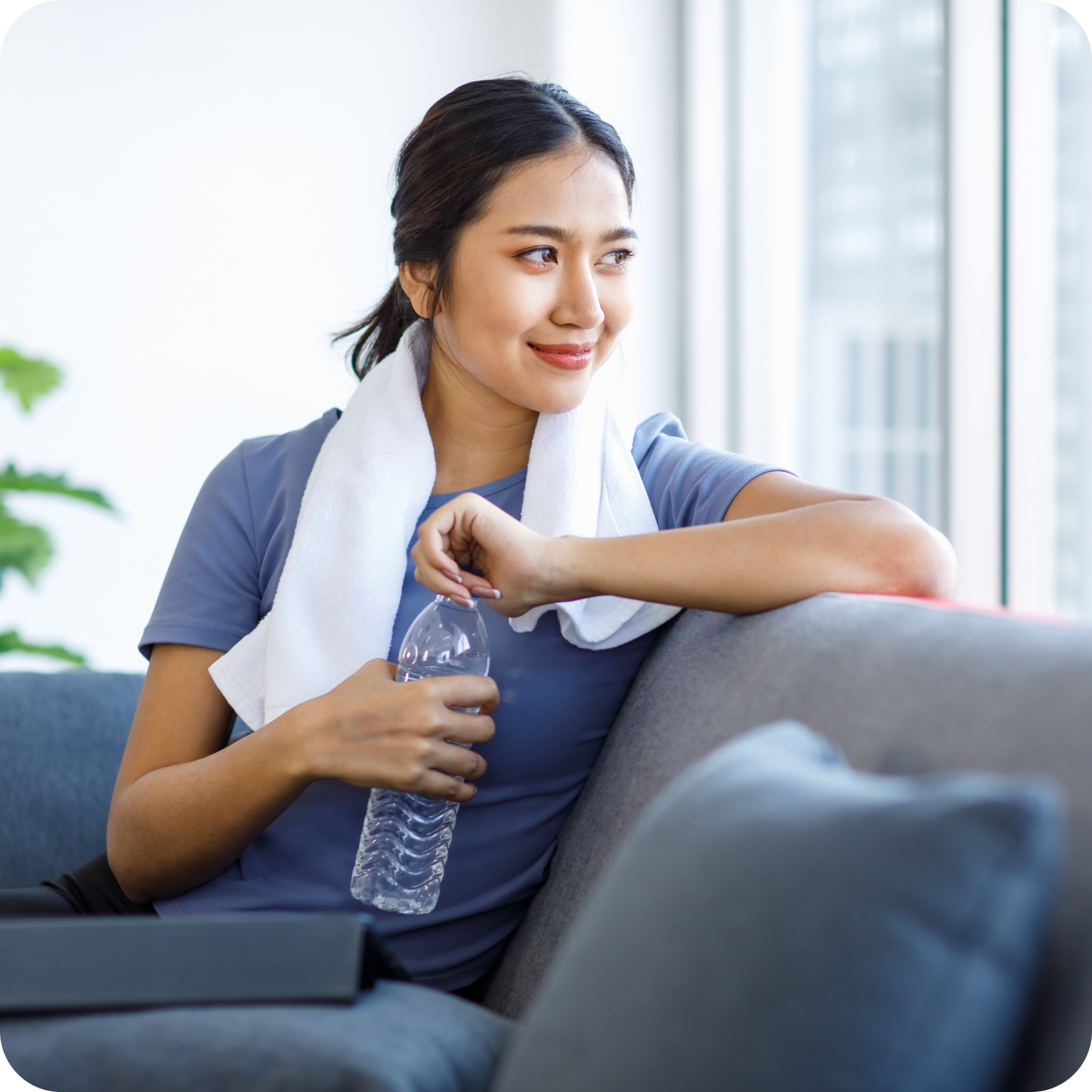 Active woman resting with towel and water bottle, staying hydrated after workout indoors