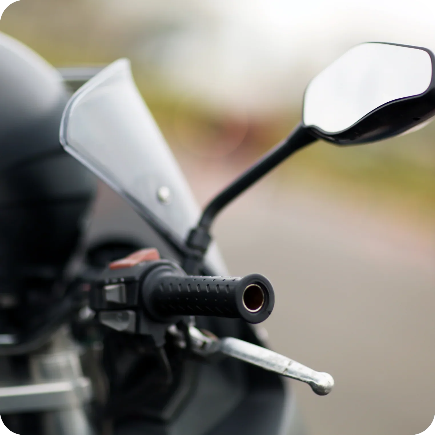Close-up of motorcycle handlebar grip, mirror, and control lever outdoors