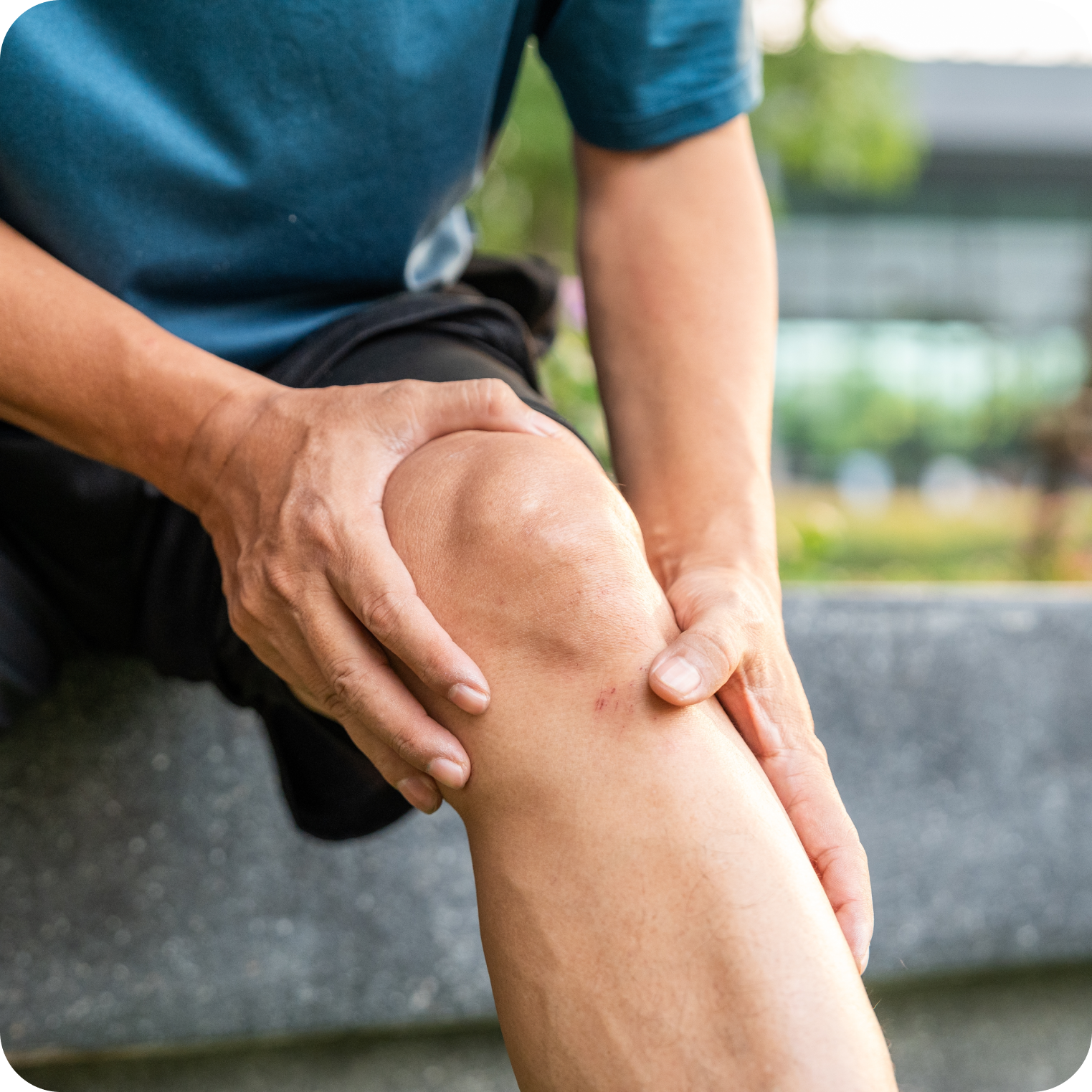 Active person holding sore knee outdoors, possible muscle cramp or dehydration