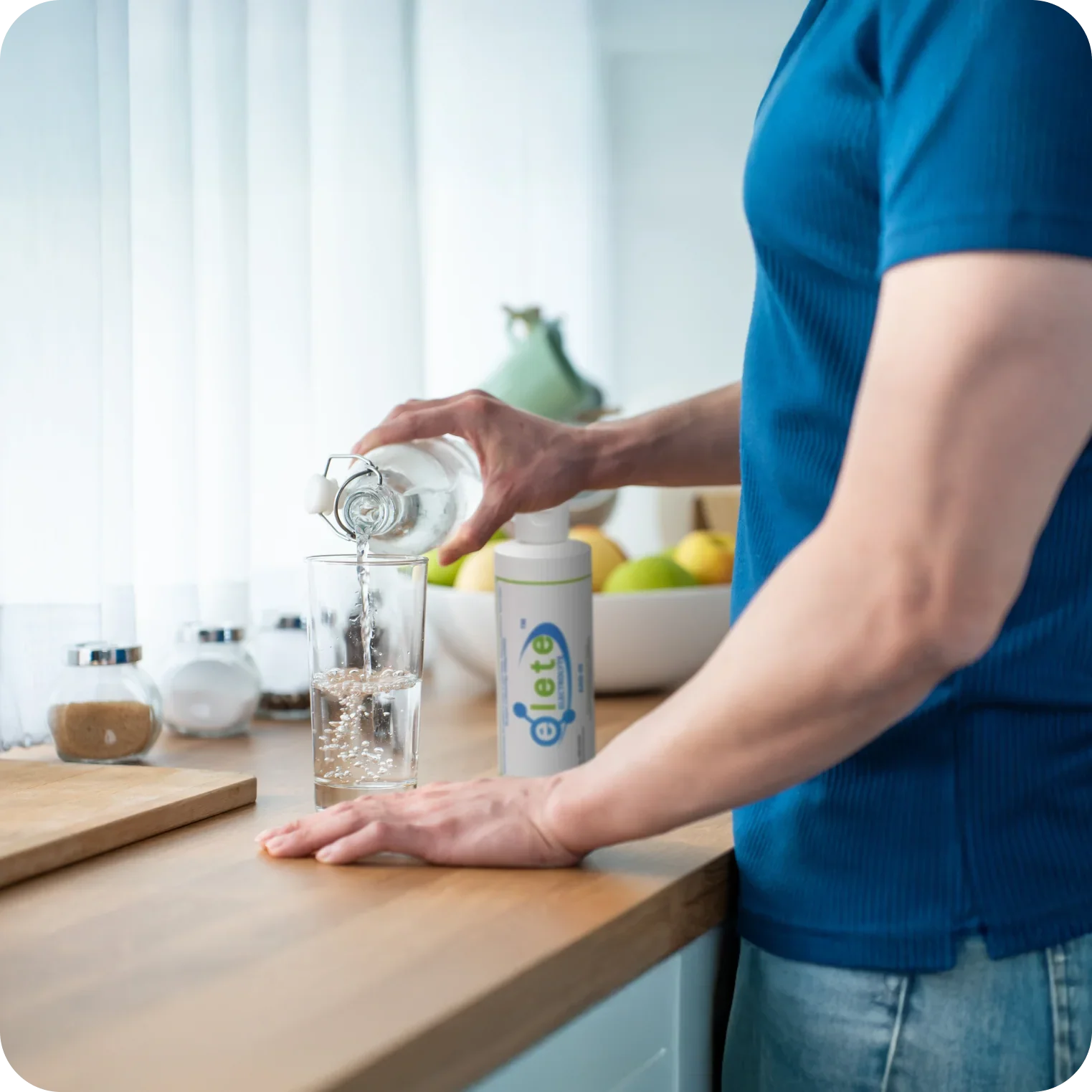 Person pouring water into glass next to natural electrolyte concentrate in kitchen