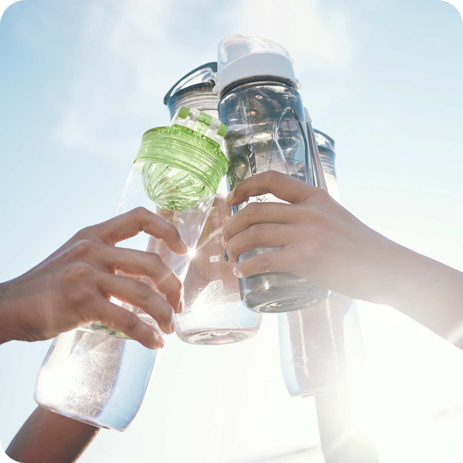 Hands toasting reusable water bottles outdoors, promoting hydration and electrolytes